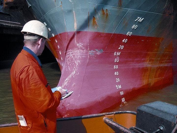 Surveyor recording draught marks on a vessel hull from a boat