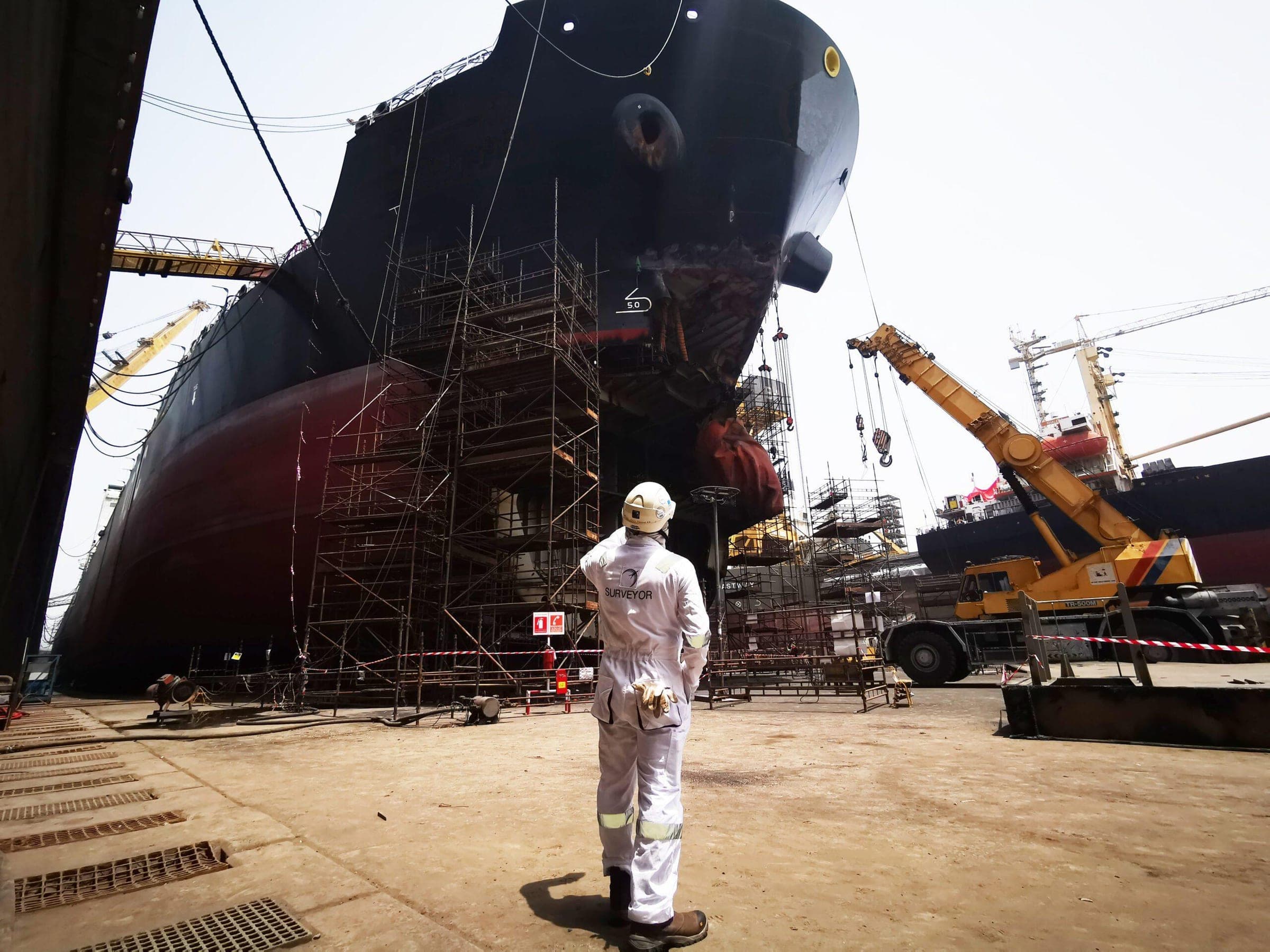Surveyor looking up at a vessel under construction in the yard